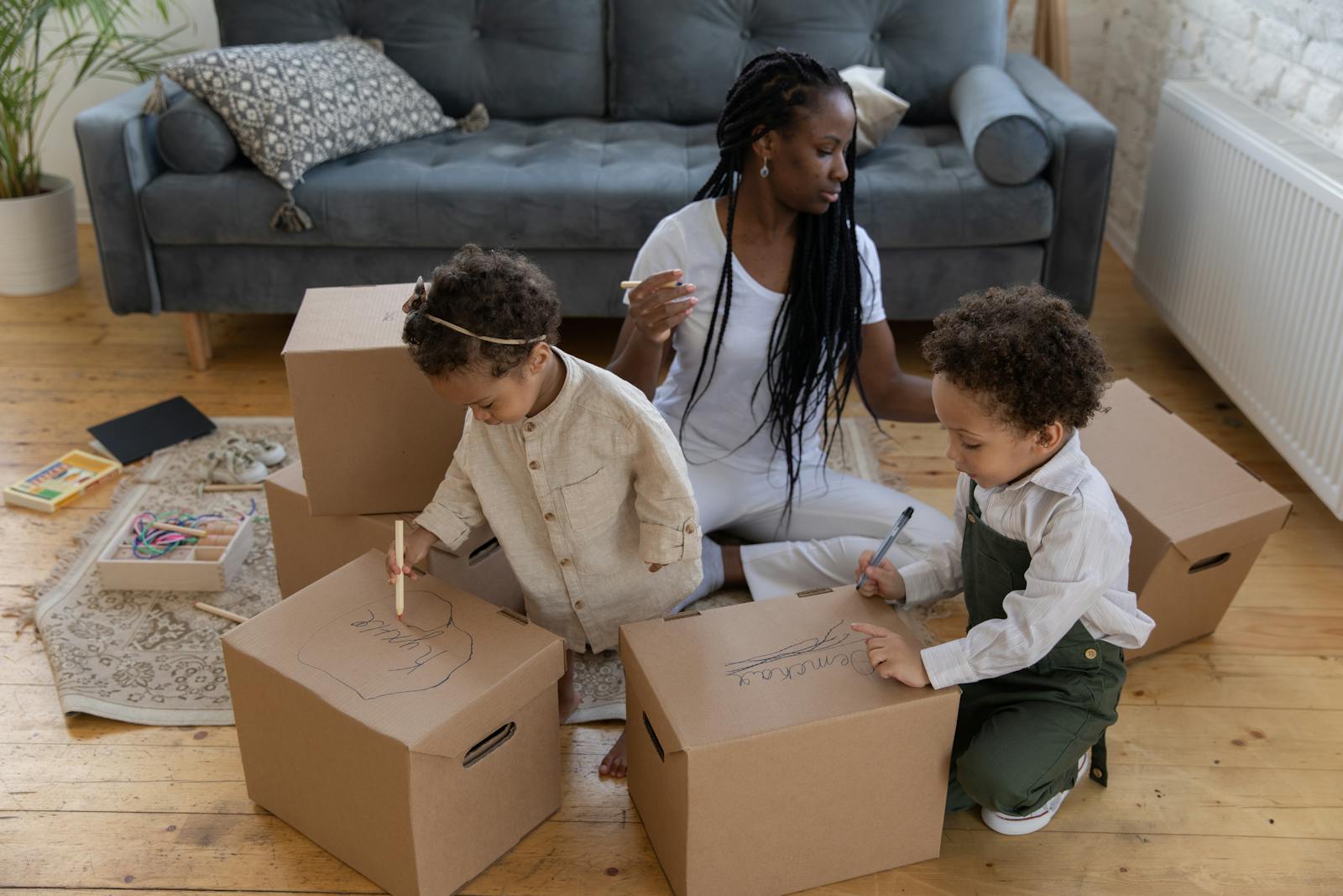 A woman and children enjoy creative art time, drawing on cardboard boxes indoors.