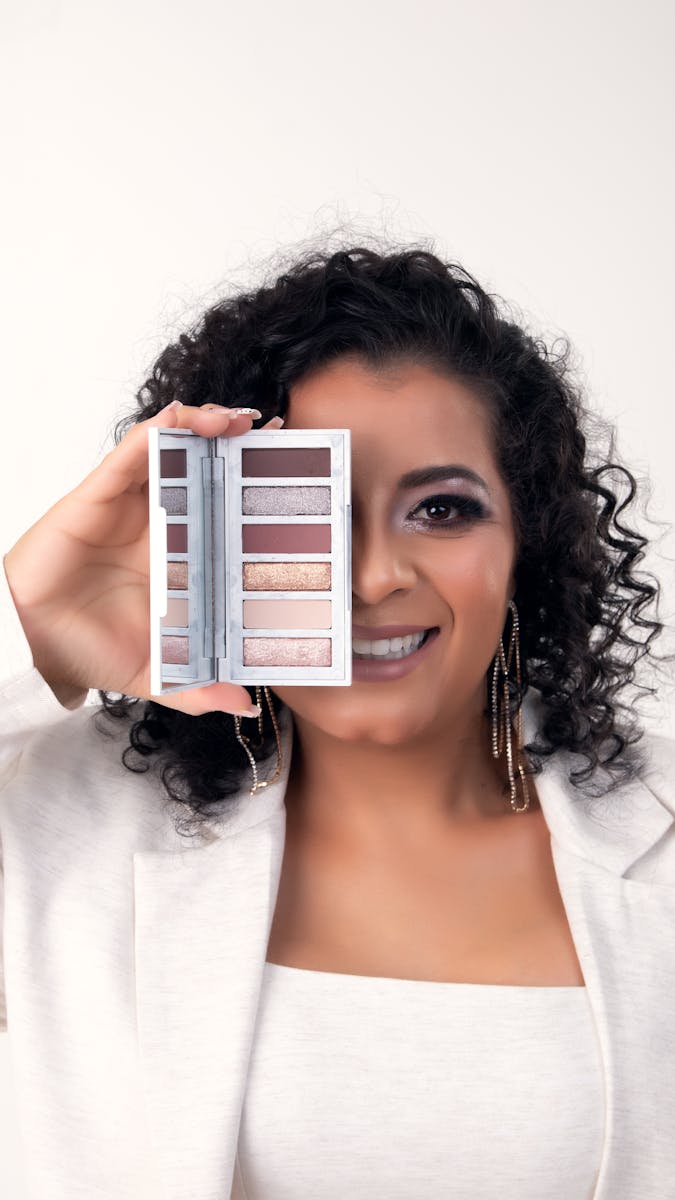 Woman showcasing an eyeshadow palette with a smile, perfect for beauty and makeup themes.