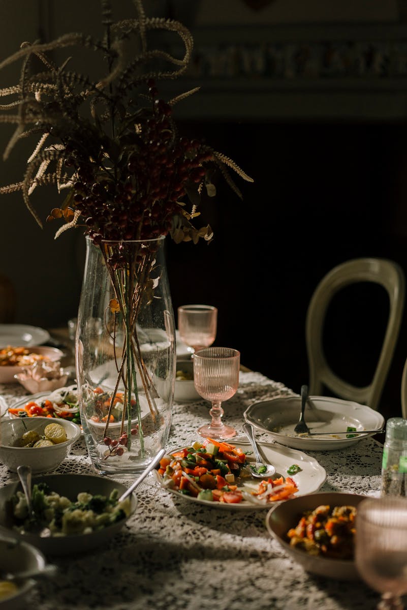 A beautifully set dining table adorned with assorted vegetable dishes, glassware, and a vase centerpiece.