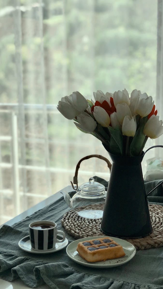 A cozy breakfast scene with coffee, waffles, and tulips by the window.