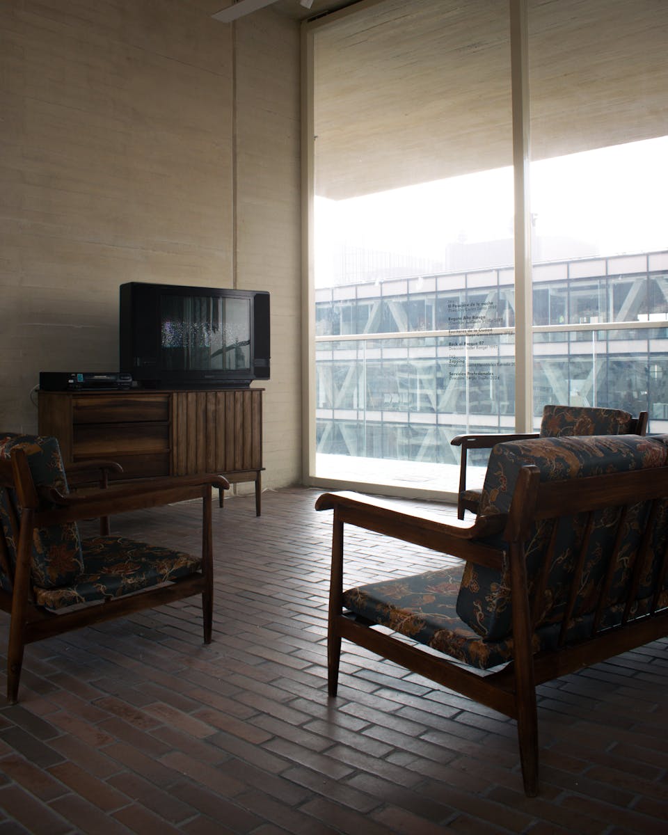 Mid-century modern room with vintage furniture overlooking cityscape through large windows.