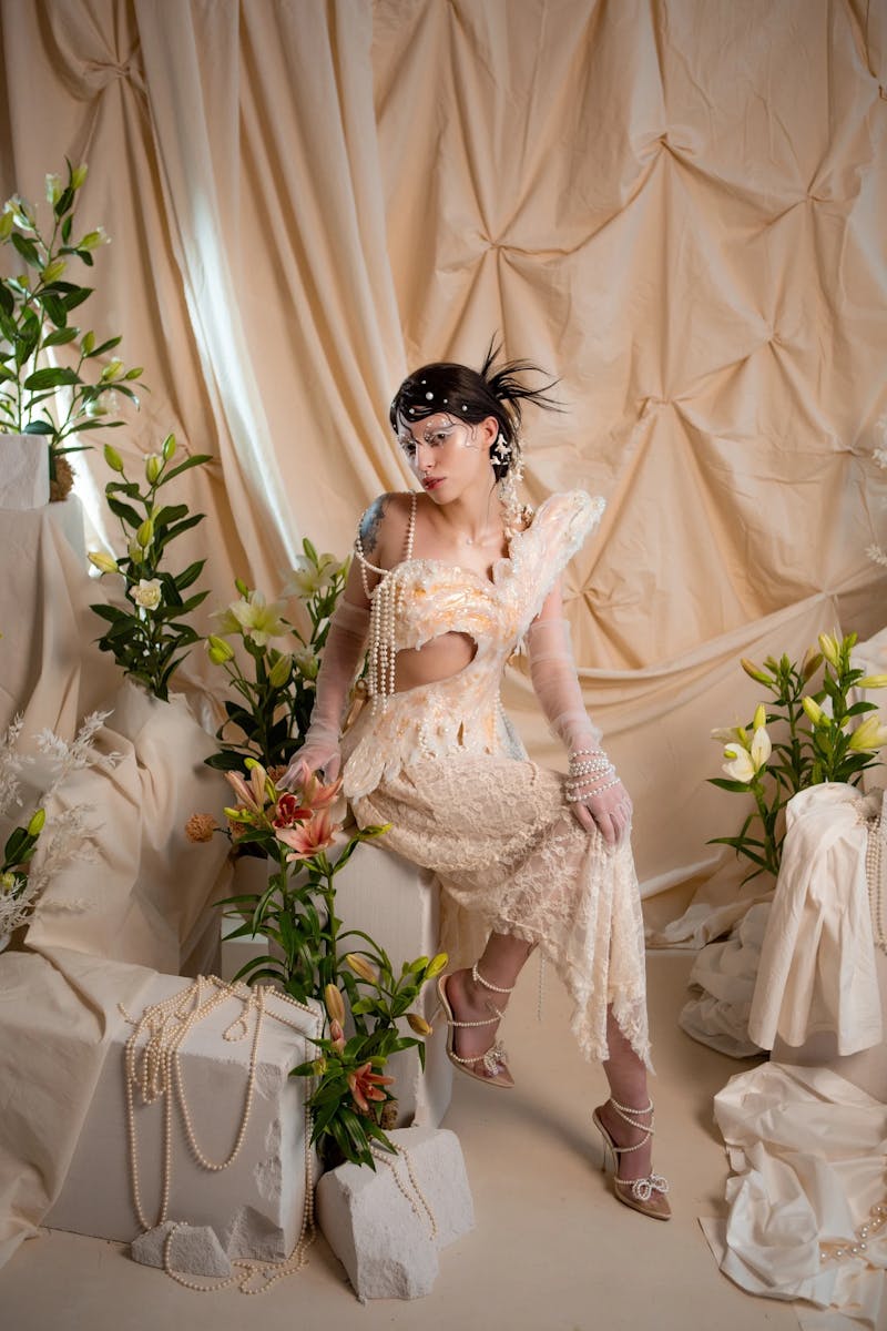 Fashionable woman in vintage attire surrounded by lilies and draped fabric.