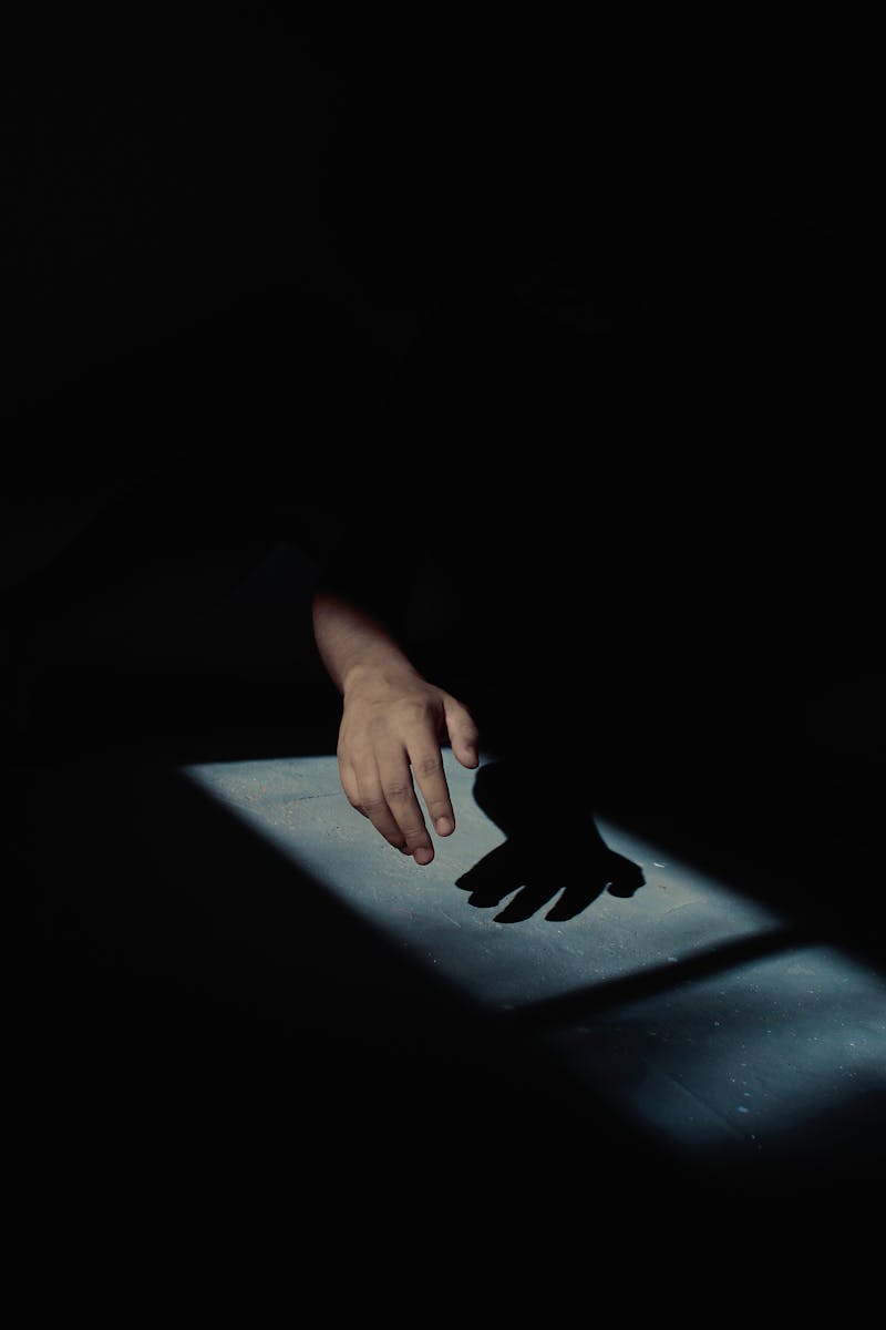 Silhouette of a hand in dramatic low-light casting a shadow. High contrast effect.