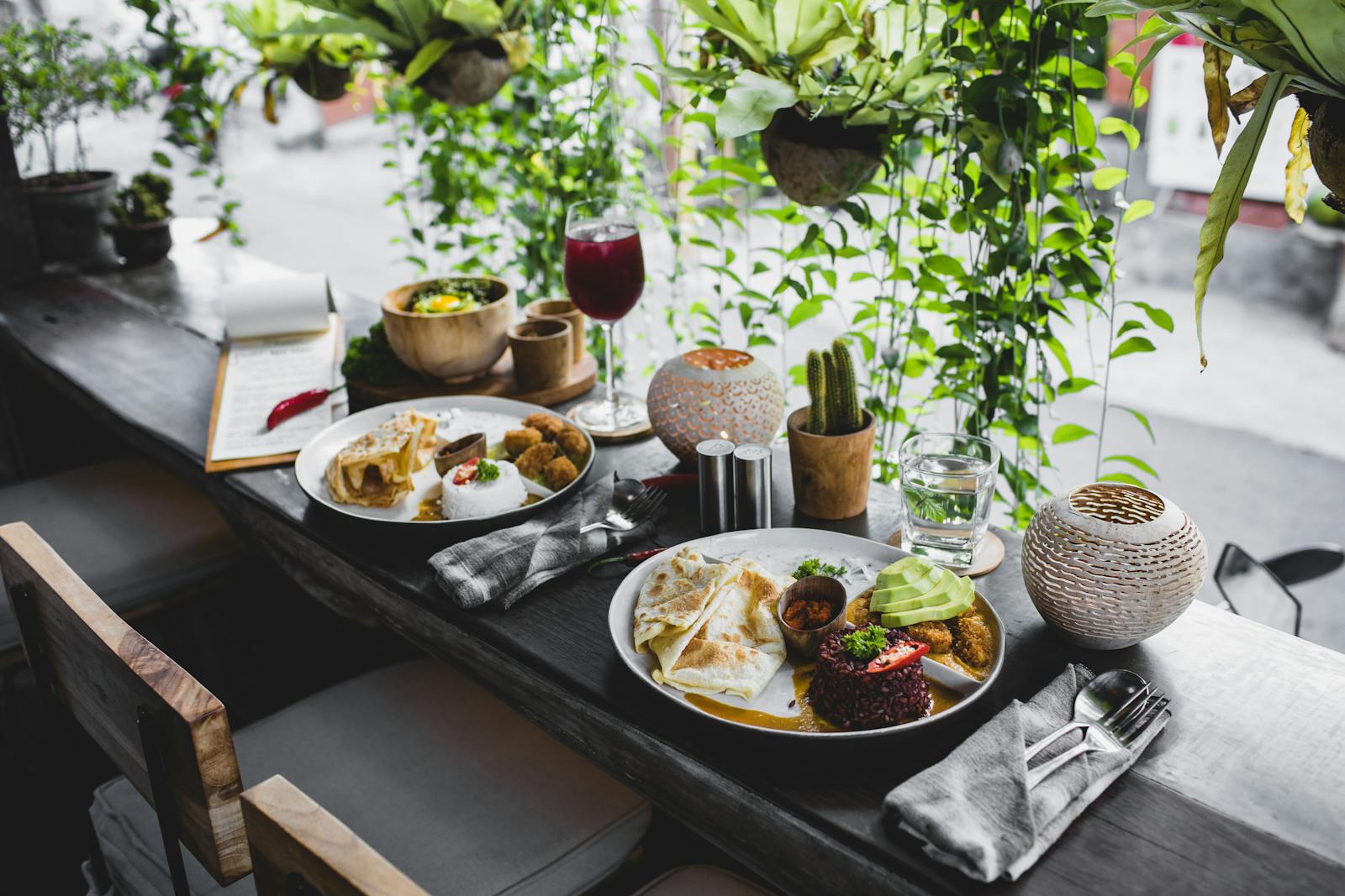 High angle of plates with assorted healthy dishes served on wooden table with cutlery and drinks in stylish tropical cafe