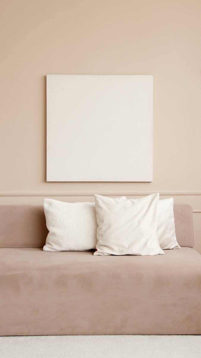 A minimalist living room with a beige sofa and a blank canvas on a neutral wall.