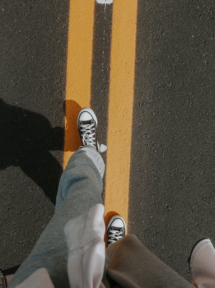Overhead shot of casual walk on road with sneakers and yellow line, showcasing perspective.