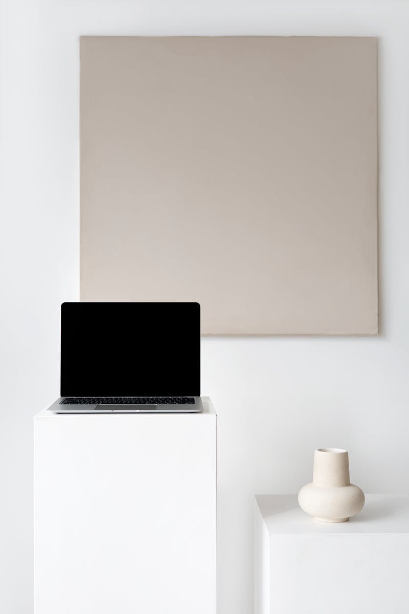 A minimalist office setup featuring a laptop with a black screen and ceramic vase on pedestals, ideal for modern themes.