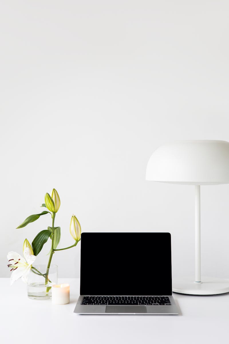 A modern minimalist workspace featuring a laptop, white lamp, and fresh flowers on a desk.