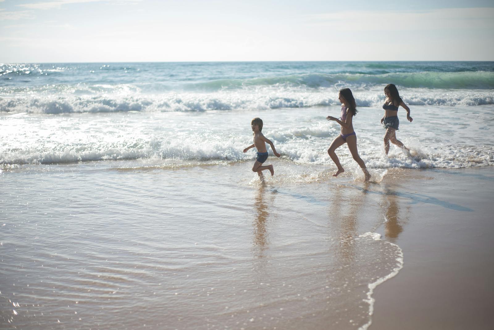 Joyful children running through waves on a sandy beach during a warm summer day.