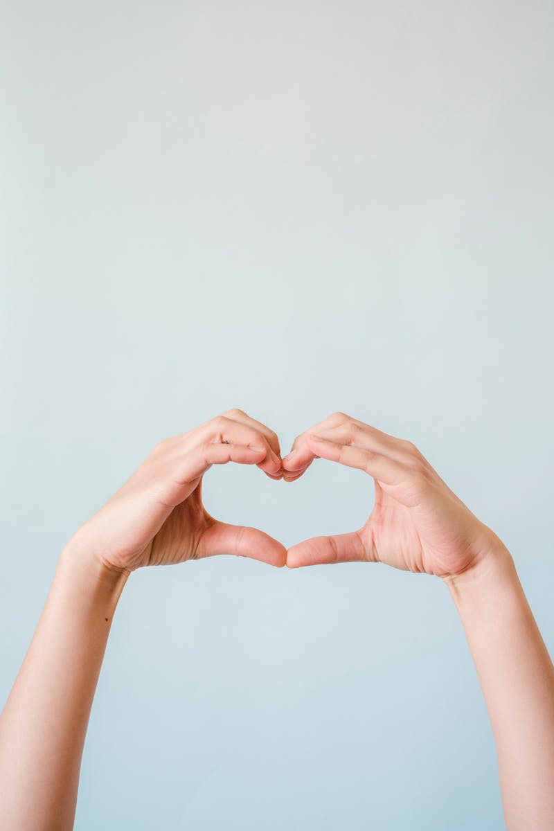 Two hands creating a heart shape against a clean, minimalist backdrop symbolizing love and connection.